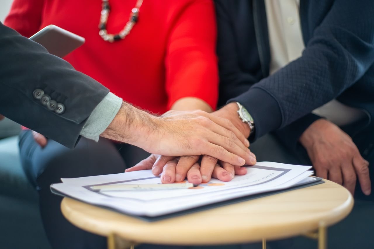 our-story-02 Business professionals collaborating, with hands united over important documents, symbolizing teamwork and unity.